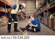 A warehouse worker consoles and helps a female worker who cries out in pain after a leg accident in a large warehouse. Стоковое фото, агентство Ingram Publishing / Фотобанк Лори