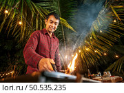 Portrait of Happy Asian young man cooking meat on barbecue grill at new year party. Bar-B-Q or BBQ on traditional stove. Night Party, people and celebration concept. Стоковое фото, агентство Ingram Publishing / Фотобанк Лори