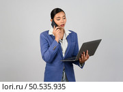 Portrait Asian young woman in officer uniform standing posture talking with mobile phone during working with laptop computer in hand,  isolated on white background. Стоковое фото, агентство Ingram Publishing / Фотобанк Лори