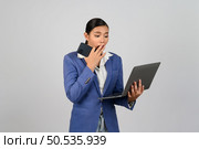 Portrait Asian young woman in officer uniform standing posture talking with mobile phone during working with laptop computer in hand with feel exciting,  isolated on white background. Стоковое фото, агентство Ingram Publishing / Фотобанк Лори
