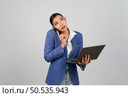 Portrait Asian young woman in officer uniform standing posture talking with mobile phone during working with laptop computer in hand,  isolated on white background. Стоковое фото, агентство Ingram Publishing / Фотобанк Лори
