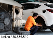 A auto mechanic checking the condition of a car’s brake discs and the condition of the tires that have been used for a while. Стоковое фото, агентство Ingram Publishing / Фотобанк Лори