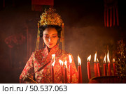 Chinese woman make wishes, pray, and light candles. On the occasion of the annual Chinese New Year festival, in a revered shrine or temple, And in Chinese where candles mean good luck and happiness. Стоковое фото, агентство Ingram Publishing / Фотобанк Лори