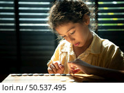 Portrait of a little girl in office room of house with a game of Go being learned to build concentration and intelligence. Стоковое фото, агентство Ingram Publishing / Фотобанк Лори