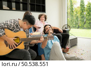 Multiethnic group of friends having fun playing guitar and singing together at home. Стоковое фото, агентство Ingram Publishing / Фотобанк Лори