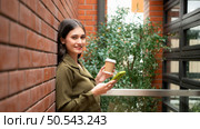 Portrait of a beautiful young woman drinking coffee and using mobile phone while leaning on a brick wall. Стоковое фото, агентство Ingram Publishing / Фотобанк Лори