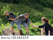 Group of friend on a sunny day in the forest Young group hiker with backpack and trekking poles helping to pull each other up to stand on the log. Стоковое фото, агентство Ingram Publishing / Фотобанк Лори