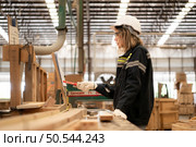 Female carpenter working in a woodworking factory, She is wearing a safety helmet and glasses. Checking the neatness of the planks against the design documents. Стоковое фото, агентство Ingram Publishing / Фотобанк Лори