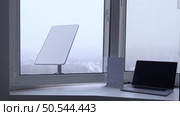KYIV, UKRAINE - JANUARY 24, 2023: SpaceX Starlink satellite dish attached outside while modern laptop and wi-fi router working inside. Reliable satellite transmission of internet.. KYIV, UKRAINE - JANUARY 24, 2023: SpaceX Starlink satellite dish attached outside while modern laptop. Редакционное фото, агентство Ingram Publishing / Фотобанк Лори