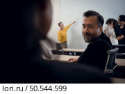 Mature guy turns to consult with attendees sitting at a table in the back of the conference room while listening to a presentation. Стоковое фото, агентство Ingram Publishing / Фотобанк Лори