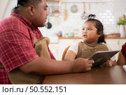 A plus-size family with a father wearing a prosthetic leg, is happily assisting a child with her homework and having fun together in the dining room of the house before cooking together. Стоковое фото, агентство Ingram Publishing / Фотобанк Лори