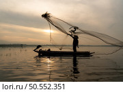 Silhouette of fisherman at sunrise, Standing aboard a rowing boat and casting a net to catch fish for food. Стоковое фото, агентство Ingram Publishing / Фотобанк Лори