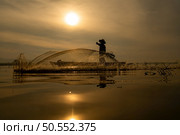 Silhouette of fisherman at sunrise, Standing aboard a rowing boat and casting a net to catch fish for food. Стоковое фото, агентство Ingram Publishing / Фотобанк Лори