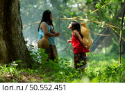 Two girls Asian women with traditional clothing stand in the rainforest. They had fun playing together before assisting Grandpa in catching fish in a nearby lake. Стоковое фото, агентство Ingram Publishing / Фотобанк Лори