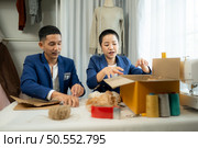 Young Asian businessman and woman Clothes are being packaged for delivery to customers in cardboard boxes and cushioned lump from natural materials that are not toxic to the planet. Стоковое фото, агентство Ingram Publishing / Фотобанк Лори