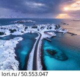 Aerial view of road, island in snow, rorbu, sea, bridge, snowy mountains, azure water, cloudy sky at sunset in winter. Dramatic landscape. Top drone view of road. Henningsvaer, Lofoten islands, Norway. Стоковое фото, агентство Ingram Publishing / Фотобанк Лори