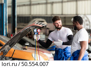Car mechanic working in an auto repair shop, inspecting the operation of the car’s air conditioner and refrigerant. Стоковое фото, агентство Ingram Publishing / Фотобанк Лори