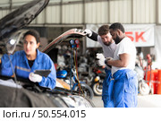 Car mechanic working in an auto repair shop, inspecting the operation of the car’s air conditioner and refrigerant, Focus on woman. Стоковое фото, агентство Ingram Publishing / Фотобанк Лори