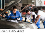 Car mechanic working in an auto repair shop, inspecting the operation of the car’s air conditioner and refrigerant, Focus on woman. Стоковое фото, агентство Ingram Publishing / Фотобанк Лори