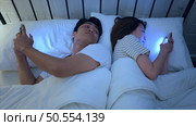Young couple sleeping on the bed in the bedroom at night time with their backs to each other and playing on their phones, ignoring each other. Стоковое фото, агентство Ingram Publishing / Фотобанк Лори