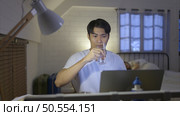 Young Asian man working overtime at home take medicine and drink water to relieve stress and headaches. Стоковое фото, агентство Ingram Publishing / Фотобанк Лори