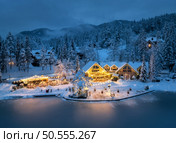 Aerial view of illuminated houses in fairy village in snow, forest, Jasna lake, street lights at winter night. Top view of alpine mountains in fog, snowy pine trees at dusk. Kranjska Gora, Slovenia. Стоковое фото, агентство Ingram Publishing / Фотобанк Лори