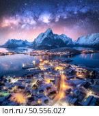 Milky Way over the snowy village, islands, rorbuer, city lights, sea, mountain, purple starry sky at winter night. Landscape with town, street illumination. Reine, Lofoten islands, Norway. Aerial view. Стоковое фото, агентство Ingram Publishing / Фотобанк Лори