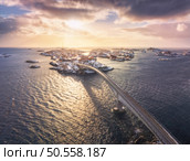 Aerial view of bridge, snowy rocks, islands with rorbu, sea, water, mountains, orange sky with clouds at sunset in winter. Beautiful landscape. Top view of road. Henningsvaer, Lofoten islands, Norway. Стоковое фото, агентство Ingram Publishing / Фотобанк Лори