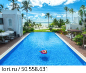 Aerial view of young woman on swimming ring in pool near ocean at sunrise. Top view of girl, blue water, beautiful hotel, palm trees, sandy beach, sea and sky with clouds. Pwani Mchangani, Zanzibar. Стоковое фото, агентство Ingram Publishing / Фотобанк Лори