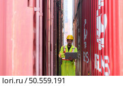 Workers in the import and export industries inspect the cargo of containers while holding a laptop and standing between them. Стоковое фото, агентство Ingram Publishing / Фотобанк Лори