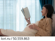 Pregnant woman reading a stories to her unborn child in the living room at home. Стоковое фото, агентство Ingram Publishing / Фотобанк Лори