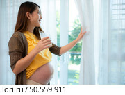 Pregnant asian woman holding glass of milk and smiles happily talking to her unborn child. Стоковое фото, агентство Ingram Publishing / Фотобанк Лори
