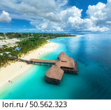 Aerial view of bungalow, white sandy beach, ocean on summer sunny day. Restaurant on the sea. Top drone view of wooden hotel, azure water, palms, sky with slouds. Luxury resort in Kendwa, Zanzibar. Стоковое фото, агентство Ingram Publishing / Фотобанк Лори