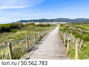 A wooden boardwalk through sand dunes leads to a coastal town of Vila Praia de Ancora nestled against hills. Стоковое фото, агентство Ingram Publishing / Фотобанк Лори