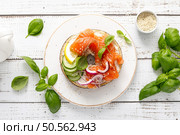 Salmon sandwiches with bagel, salted fish, fresh cucumber, onion and basil on white background, top view. Healthy breakfast with salmon toasts. Стоковое фото, агентство Ingram Publishing / Фотобанк Лори