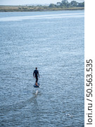 A lone surfer glides above calm waters on a hydrofoil board, surrounded by a tranquil landscape of trees and shoreline on a clear, sunny day. Стоковое фото, агентство Ingram Publishing / Фотобанк Лори