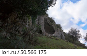 Buracas do Casmilo at Condeixa - Portugal. Ancient limestone caves nestled in a rugged hillside, featuring multiple natural cavern openings amid green vegetation and moss-covered rock formations on a cloudy day. Стоковое фото, агентство Ingram Publishing / Фотобанк Лори