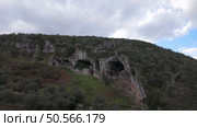 Buracas do Casmilo at Condeixa - Portugal. Ancient limestone caves nestled in a rugged hillside, featuring multiple natural cavern openings amid green vegetation and moss-covered rock formations on a cloudy day. Стоковое фото, агентство Ingram Publishing / Фотобанк Лори