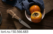 Ripe persimmons on a rustic wooden table, with a blue cloth and a cutting board. Стоковое фото, агентство Ingram Publishing / Фотобанк Лори