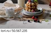 Waffles topped with fresh berries and powdered sugar sit on a stack of plates, accompanied by a jar of powdered sugar, a sifter, and a fork on a rustic table. Стоковое фото, агентство Ingram Publishing / Фотобанк Лори