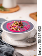 Purple soup with a pink swirl, topped with chopped nuts, pecans, and rosemary, served in a white speckled bowl on a matching plate with a spoon. Стоковое фото, агентство Ingram Publishing / Фотобанк Лори