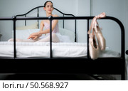 A girl ballet student warm up in bed and look at the old ballet shoes hanging from the end of the bed. Стоковое фото, агентство Ingram Publishing / Фотобанк Лори