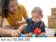 A tiny child cheerfully plays with toys on the floor of the living room with mom. Стоковое фото, агентство Ingram Publishing / Фотобанк Лори