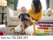 A tiny child cheerfully plays with toys on the floor of the living room with mom. Стоковое фото, агентство Ingram Publishing / Фотобанк Лори