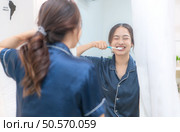 Asian young woman in a blue pajama is brushing her teeth in front of the mirror before taking a shower. Стоковое фото, агентство Ingram Publishing / Фотобанк Лори