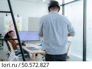 Businessman riding electric scooter in office with colleague in background. Стоковое фото, агентство Ingram Publishing / Фотобанк Лори