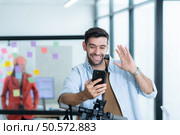 Portrait of smiling businessman talking on mobile phone while colleague using scooter in office. Стоковое фото, агентство Ingram Publishing / Фотобанк Лори