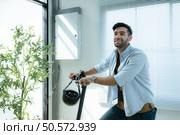 Portrait of smiling businessman with scooter while standing by window in office. Стоковое фото, агентство Ingram Publishing / Фотобанк Лори
