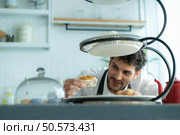 A young man puts on an apron to make dessert to eat with his wife. Checking the completeness of the finished dessert. Стоковое фото, агентство Ingram Publishing / Фотобанк Лори