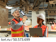 Male and female engineers work together in an electric repair station. Inspecting the undercarriage of electric train that are being repaired at the garage. Стоковое фото, агентство Ingram Publishing / Фотобанк Лори